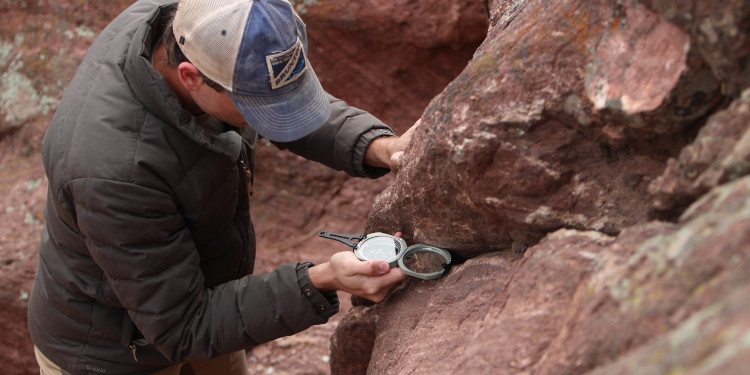 A man uses a Brunton Transit compass to take field measurements.