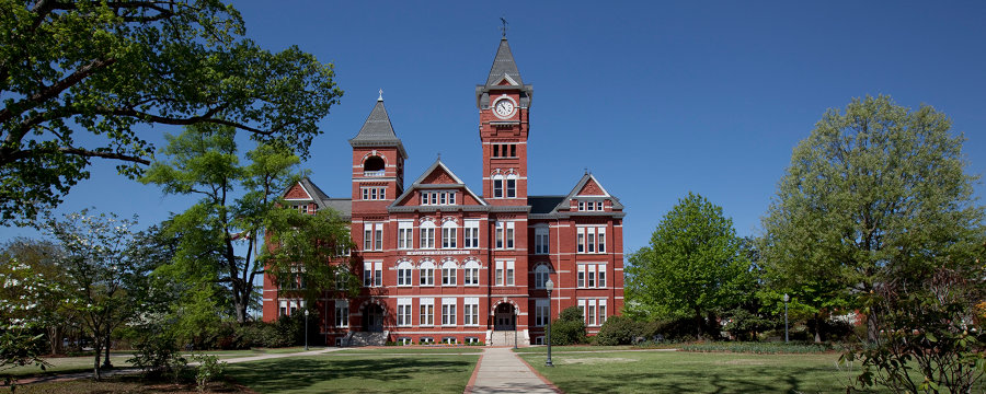 A stately red brick building rises from a well-manicured lawn crisscrossed by sidewalks.